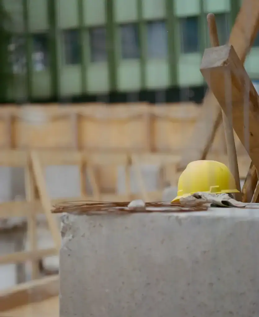 Casque jaune et gants de travail posés sur un bloc de béton devant la charpente de bois d'un chantier