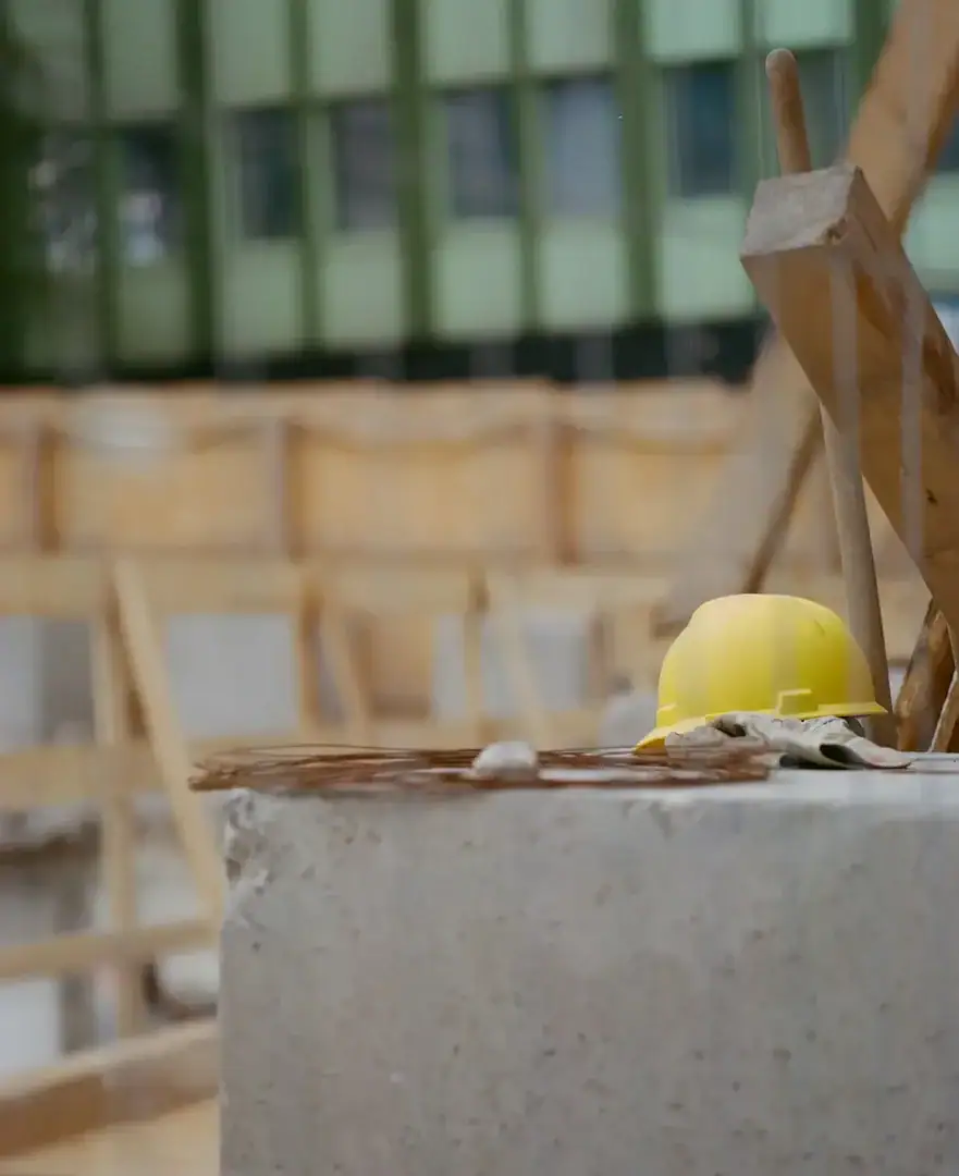 Casque jaune et gants de travail posés sur un bloc de béton devant la charpente de bois d'un chantier
