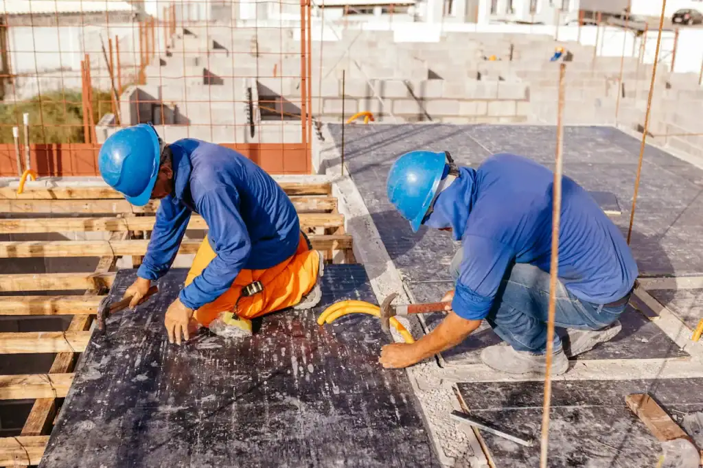 Deux ouvriers en casque bleu qui clouent le coffrage de bois d'une dalle sur un chantier de construction