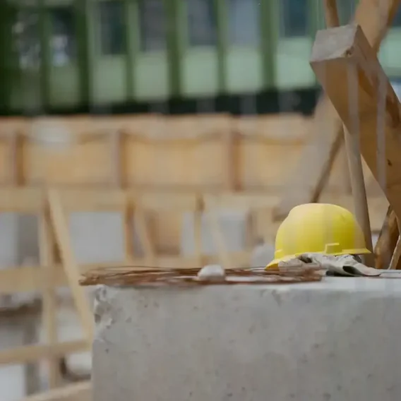 Casque jaune et gants de travail posés sur un bloc de béton devant la charpente de bois d'un chantier