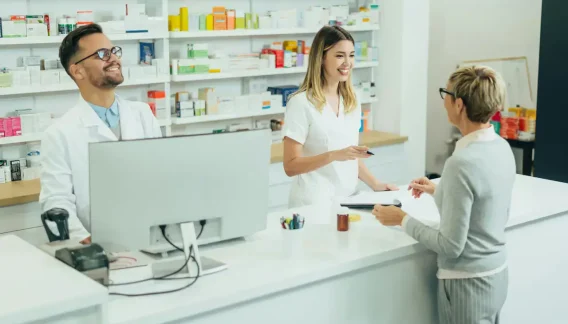 Pharmacienne et employée servant une cliente au comptoir, rayons de médicaments à l'arrière-plan