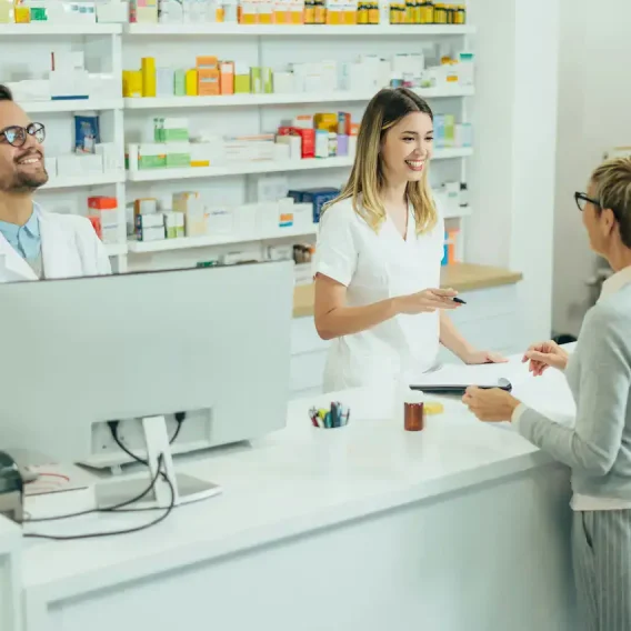 Pharmacienne et employée servant une cliente au comptoir, rayons de médicaments à l'arrière-plan