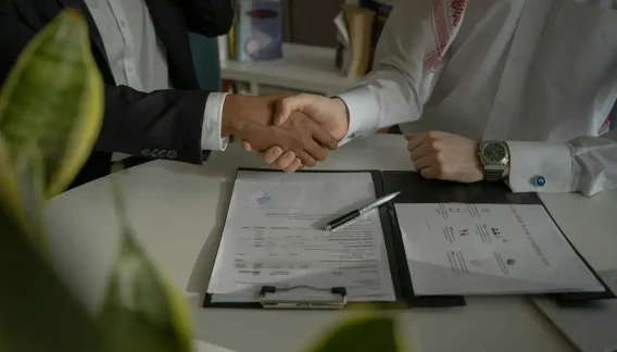 Poignée de main au-dessus d'un contrat signé, scellant un mandat avec un courtier en assurance pour entreprise