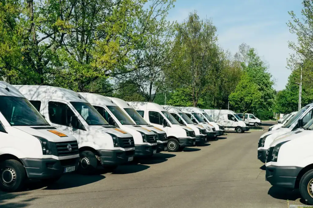 Parc de camionnettes blanches d'entreprise stationnées en rangée dans une cour asphaltée