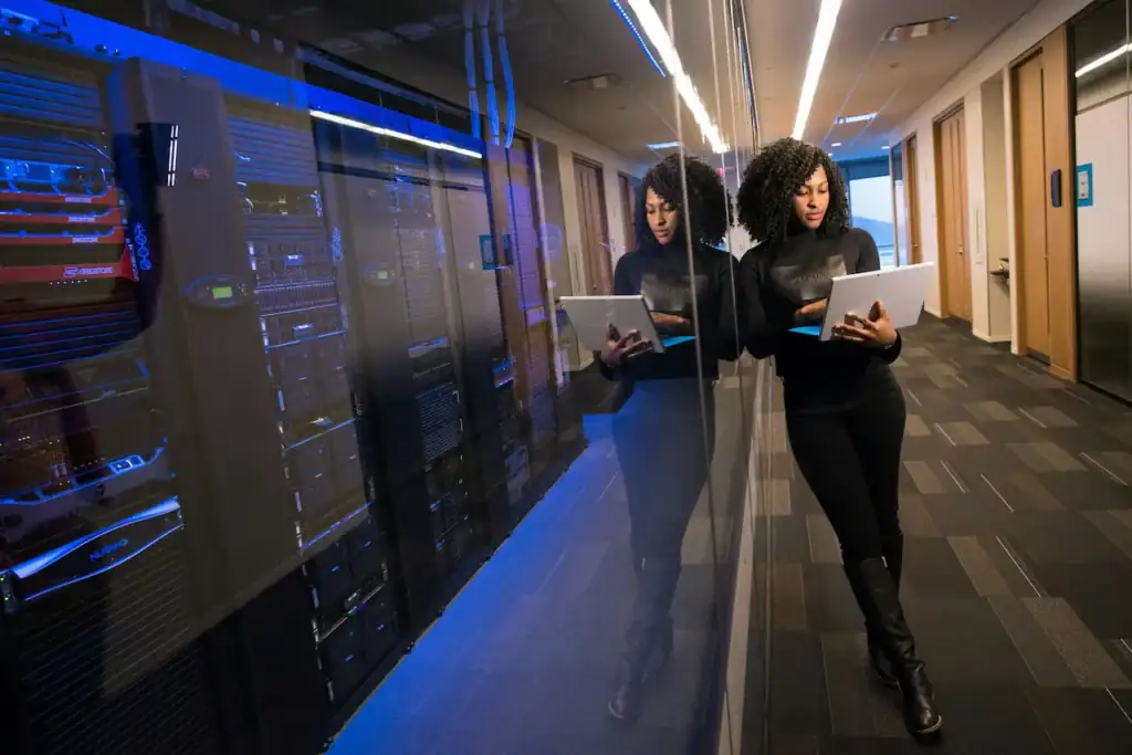 Employée qui consulte une tablette dans le corridor vitré d'une salle de serveurs aux baies éclairées de bleu